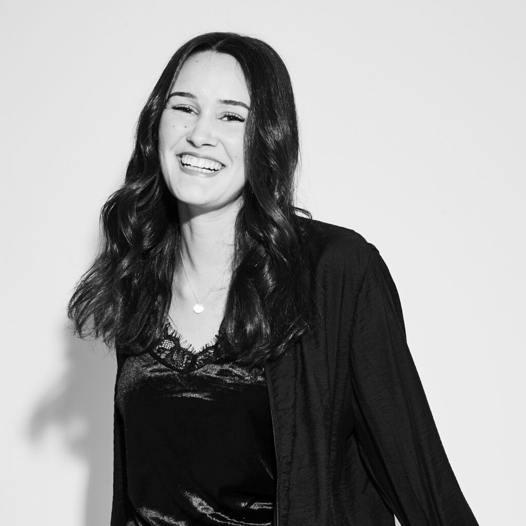 A young woman with long dark hair is laughing enthusiastically and happy in the camera. The photo is in black and white.