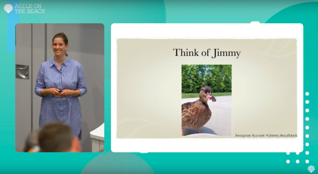 A screenshot from the talk. On the left side is a middle aged woman (Madita) in a blue/white striped dress smiling at the audience. On the right is a slide with a duck on it. The text above says "This is Jimmy". The duck is brown and has a beak that is deformed. The upper beak is next to the lower beak so that you can see her tongue.